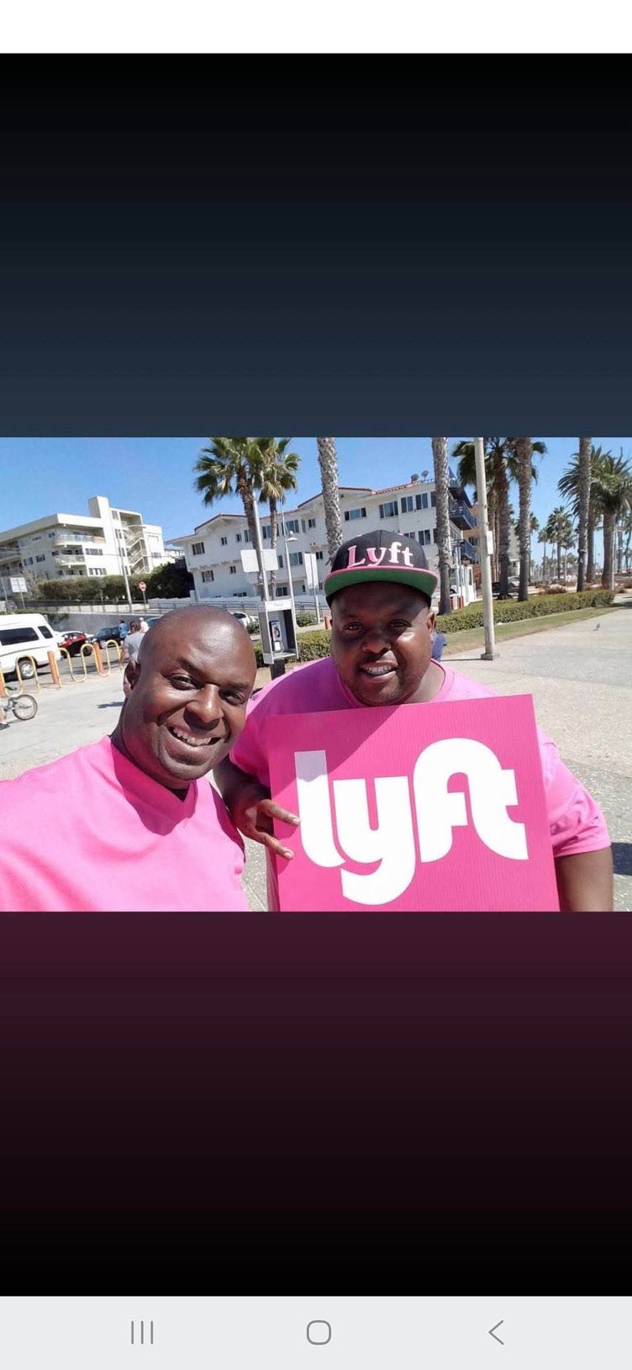Lyft team members holding a large pink Lyft sign near the Santa Monica boardwalk